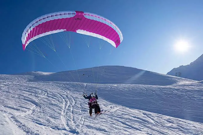 Duo en speed riding biplace sous une voile rose, glissant sur une pente enneigée