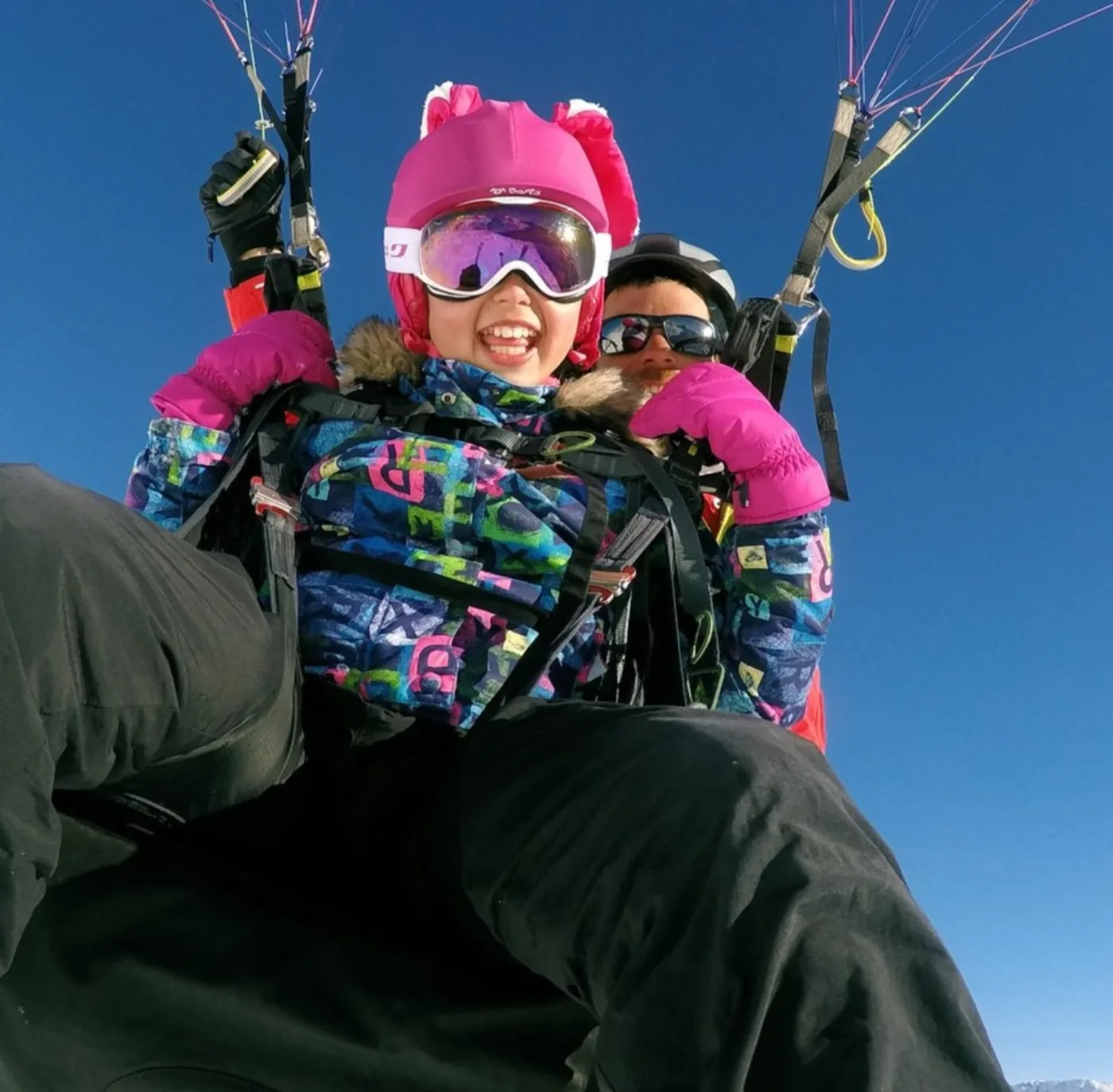 Petite fille au casque rose hilare pendant son baptême de parapente à Tignes